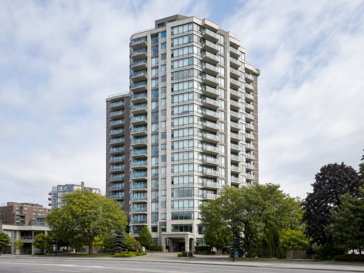 Glass residential tower with balconies rising above surrounding trees and lower buildings